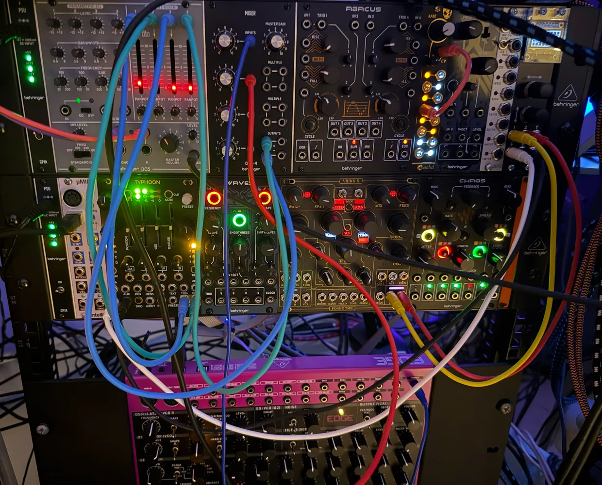 Modular synthesiser modules joined by a tangle of coloured patch cables and glowing lights.