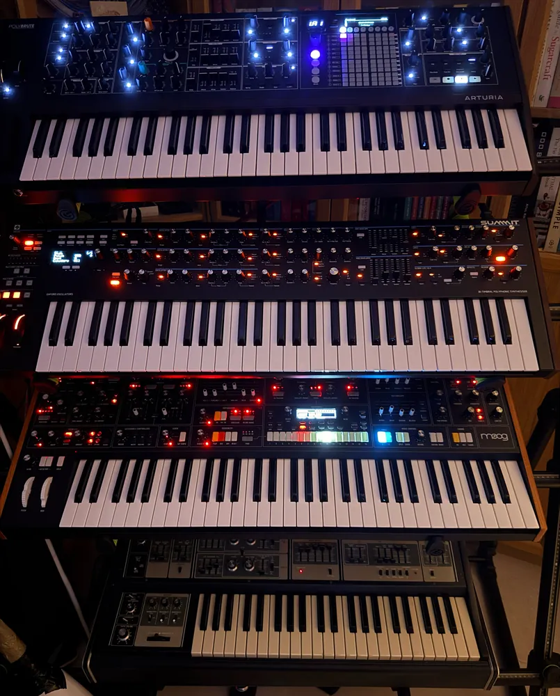 Four keyboards stacked on a tall stand, their controls lit in the dark.