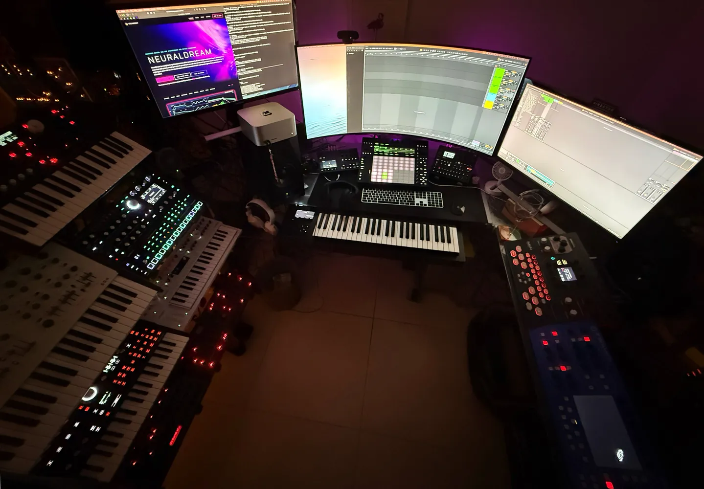 The whole studio from behind the chair, with keyboards on both sides and three screens around the desk.