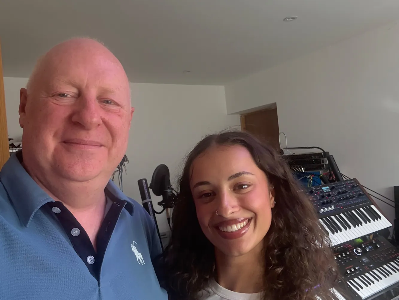 Chris in the studio with a smiling young woman, with keyboards and synthesisers behind them.